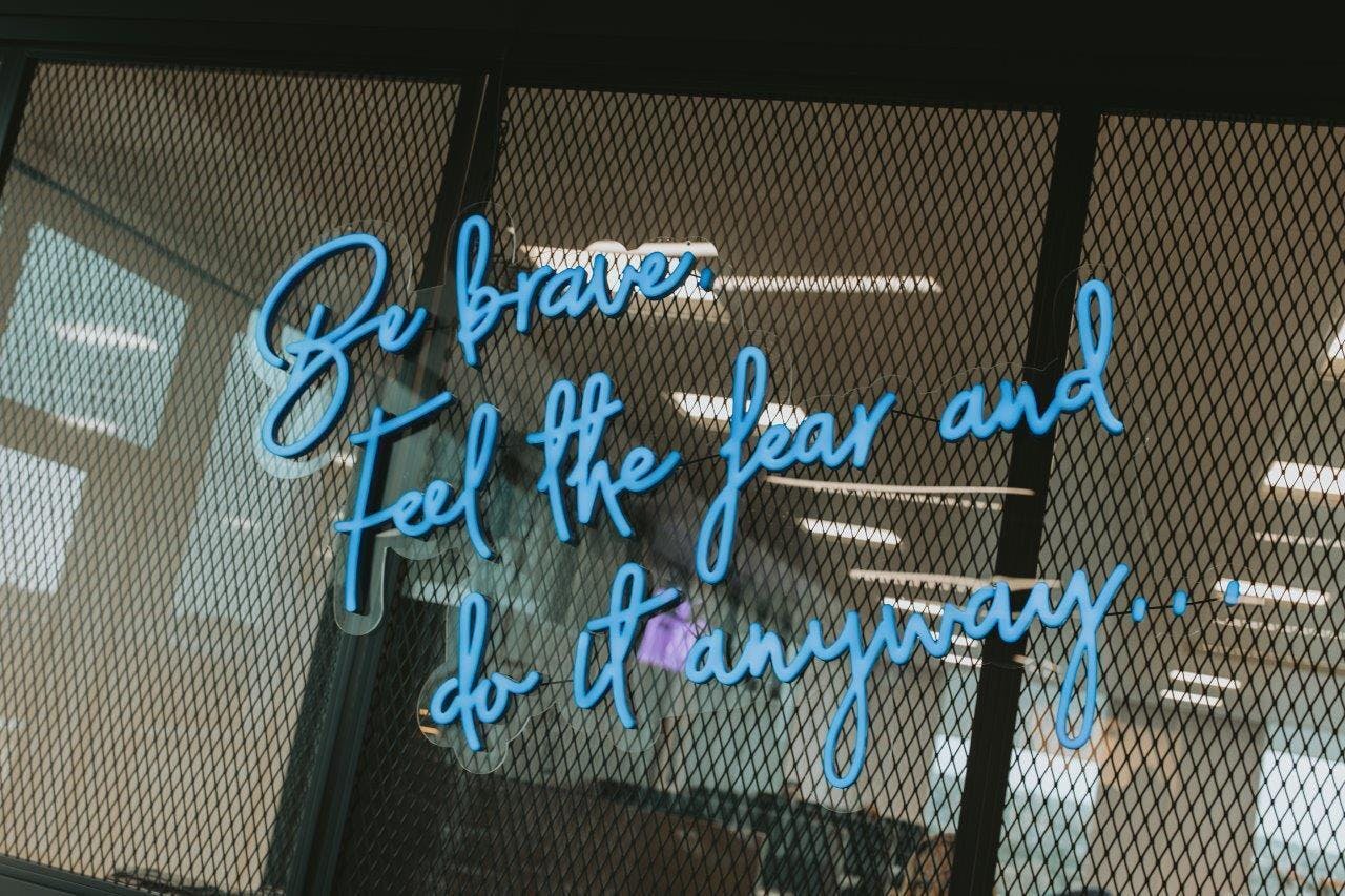 Aiimi's neon blue sign capturing one of our core values: 'Be Brave. Feel the fear and do it anyway.'